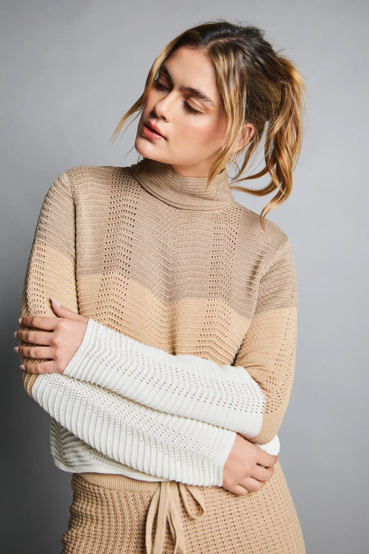 Mujer usando suéter tejido de punto en tonos beige y blanco, moda femenina elegante.